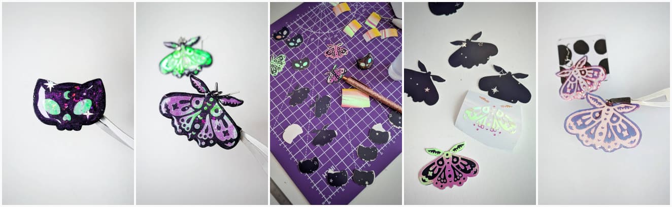 A black cat head skeleton with a moon on its forehead, a pair of moth earrings, the pieces before getting glued together, the moths with some vinyl still on the wrapper, and some purple blue moth earings made with transparent PVC 
